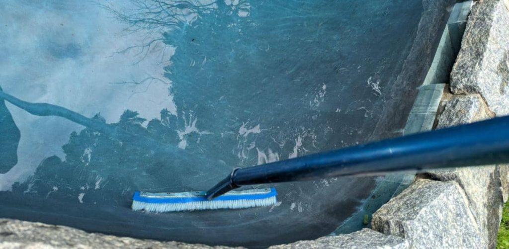 Using a pool brush to brush the sides and walls of a swimming pool